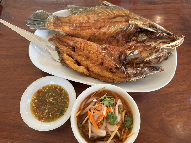 ปลาทอดกรอบสองตัวบนจาน วางคู่น้ำจิ้มรสจัดและยำผักสด